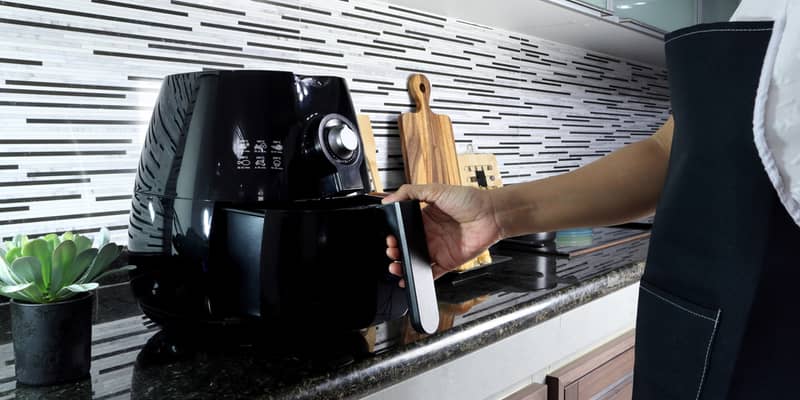 woman is holding the tray of the air fryer or oil frying machine which is on the marble table of the modern interior design kitchen