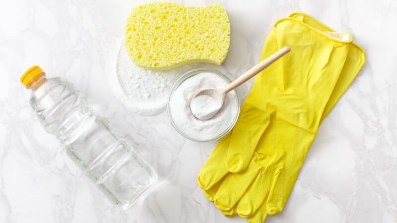 baking soda, vinegar, gloves, and sponge on top of a kitchen counter