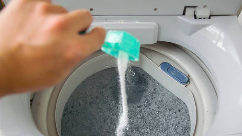 Person adding baking soda into washing machine to wash clothes for brighter and cleaner finish