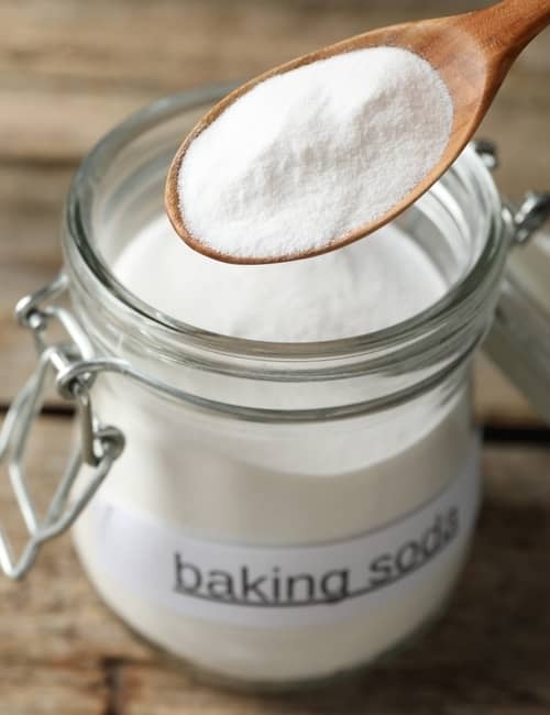 wooden spoon scooping baking soda from an open jar