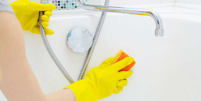 A woman cleaning bath at home. Female washing bathtub and faucet