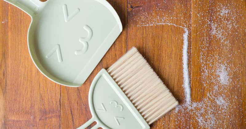 A sweeping brush with artificial bristles and a dustpan against the background of the vinyl floor covering in the kitchen close up during cleaning.