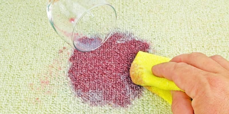 Cleaning up a spilled glass of red wine on a carpet with a cloth