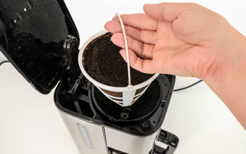 Woman hand removing mesh basket filter full of used ground coffee from drip-type coffee maker