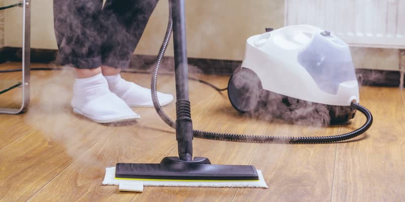 Woman cleaning the floor in the room with a white steam cleaner