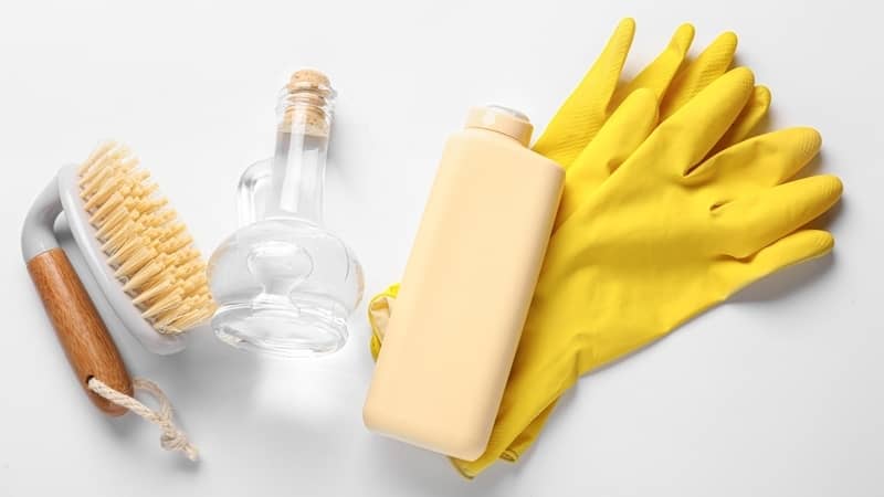 Decanter of vinegar, dish soap, brush and rubber gloves on white background