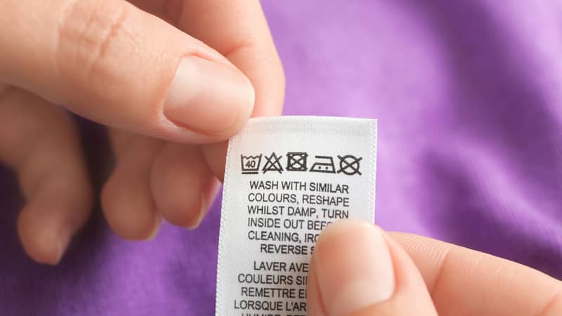 Woman reading clothing label with care instructions on pink garment, closeup