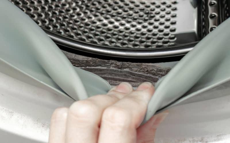 hand checking underneath the rubber gasket of a front load washing machine