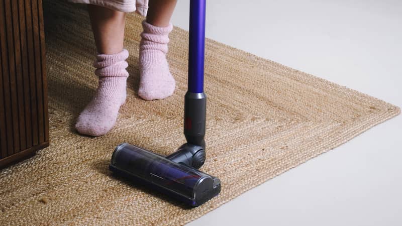 Woman cleans the flooring in the room with a hand vacuum cleaner