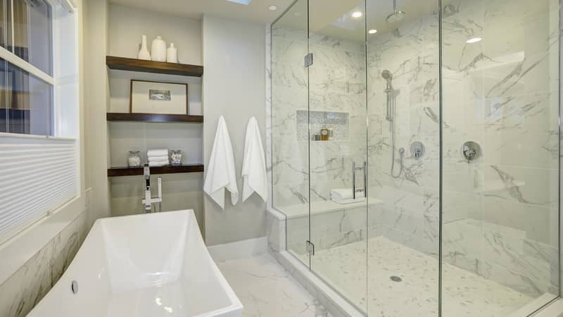 White and gray marble master bathroom with large glass walk-in shower, freestanding tub and skylights on the ceiling.