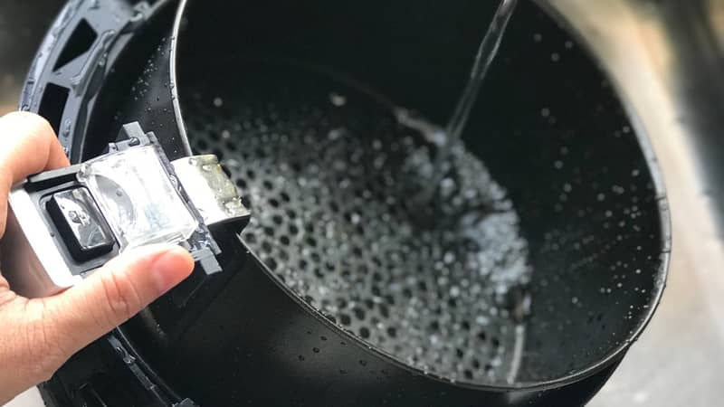 Woman’s hand holding the handle air fryer’s basket for washing