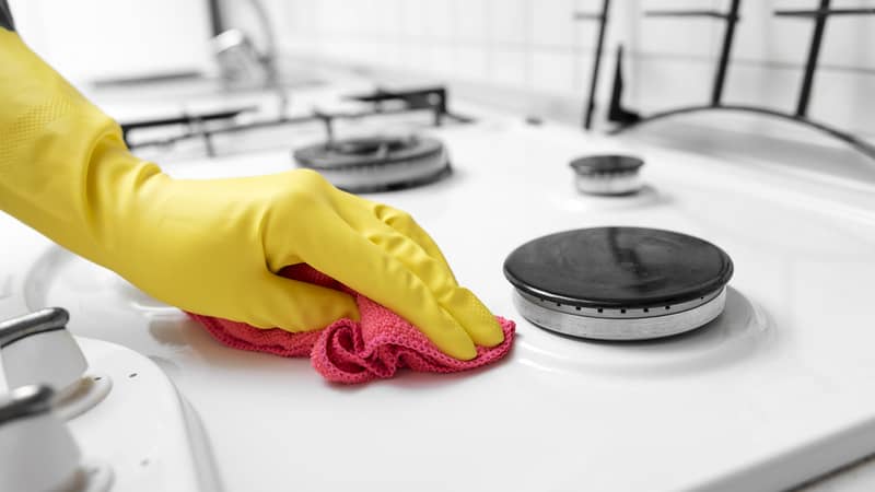 Hands in yellow gloves wiping the gas stove