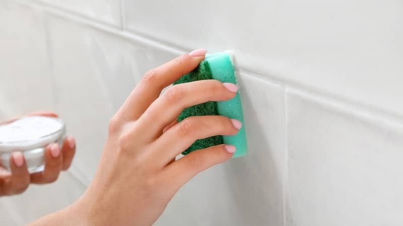 Woman cleaning tile with sponge and baking soda, closeup