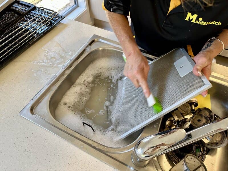 professional cleaner brushing range hood filter in the sink