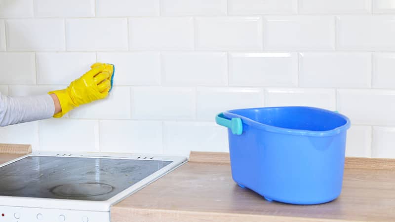 woman washes white tiles on a wooden board has a blue bucket