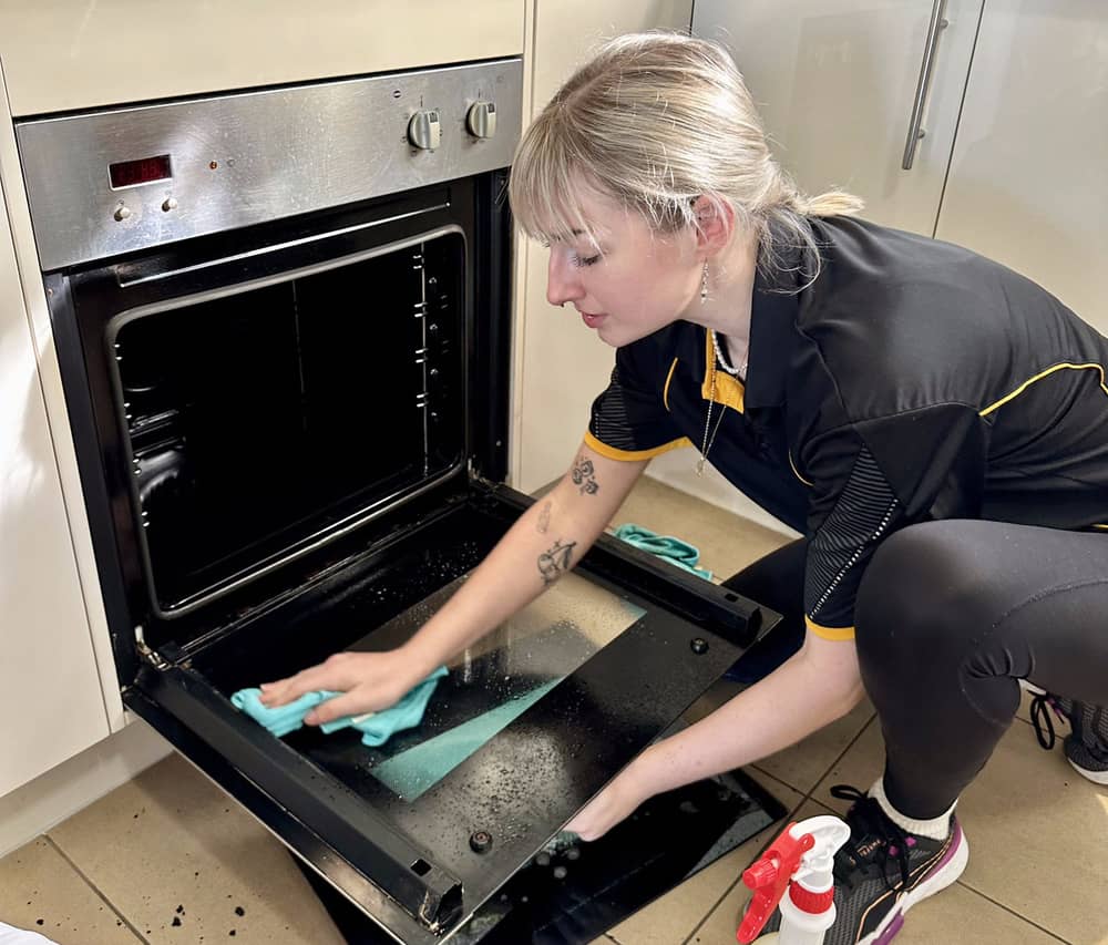 Professional cleaner cleaning inside oven glass door