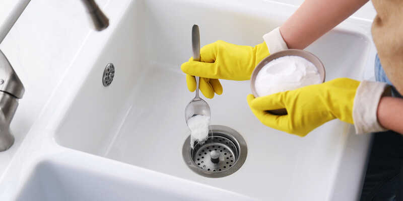 woman in yellow gloves putting baking soda in the sink