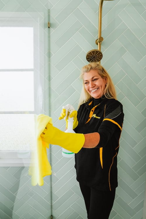 A cleaning professional using cloth and spray bottle to clean the shower area