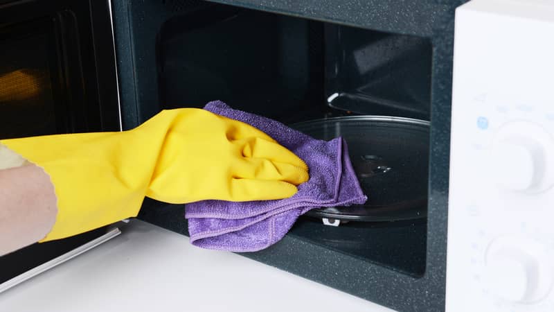 female hand with yellow gloves cleaning the interior of the microwave oven