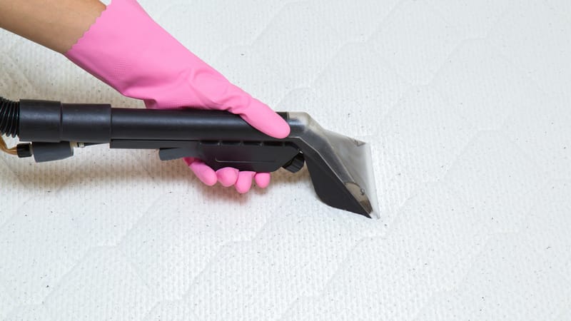 hands with gloves using vacuum to clean the mattress after removing the stains