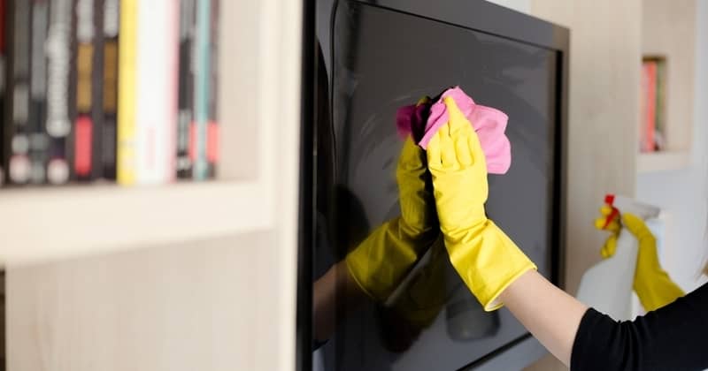 Woman in yellow rubber gloves cleaning tv with pink cloth