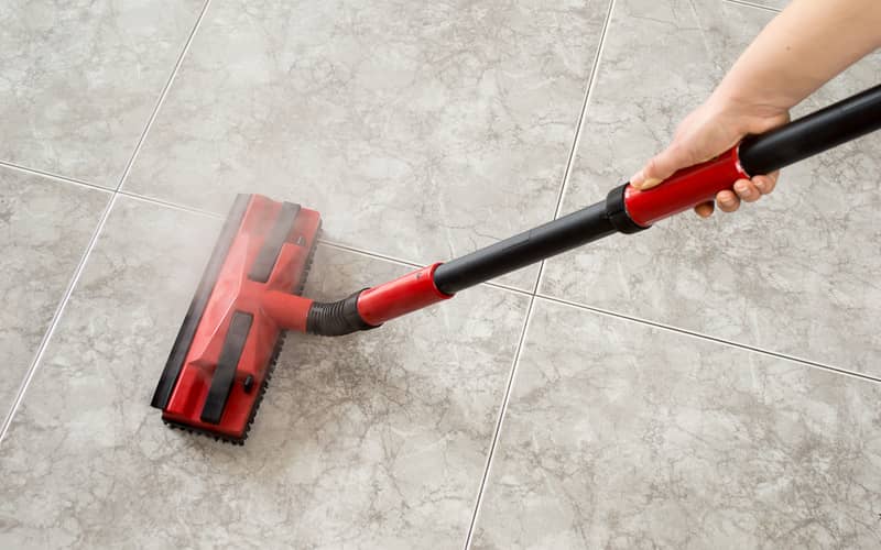 person using a red steam mop to clean tiled flooring