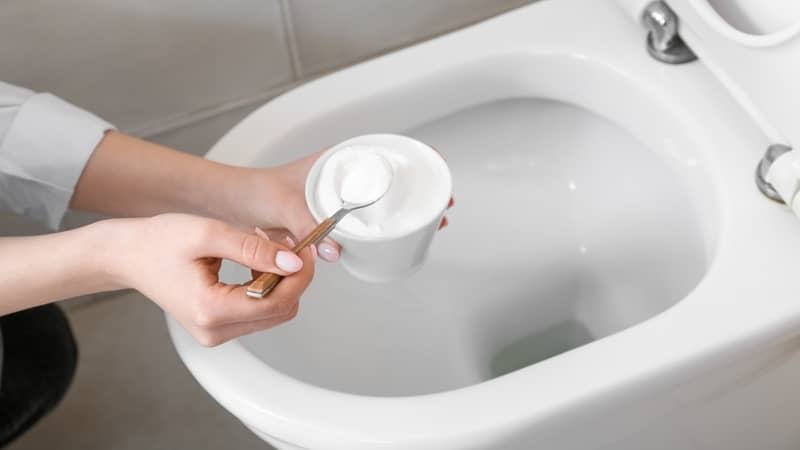 Woman sprinkling white toilet bowl with baking soda