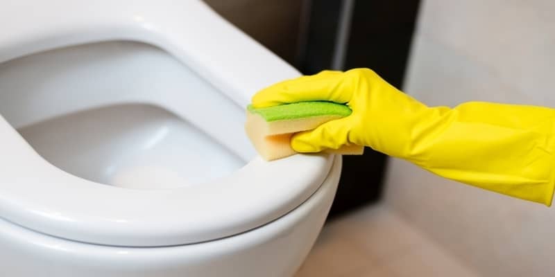 Hands with yellow rubber gloves cleaning toilet with yellow sponge