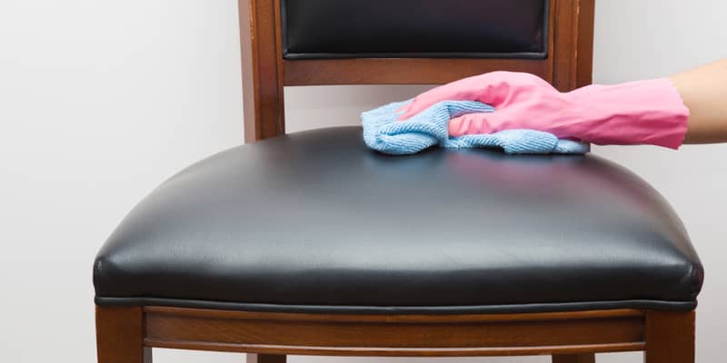 hand in rubber protective glove with microfiber cloth cleaning a black leather chair.