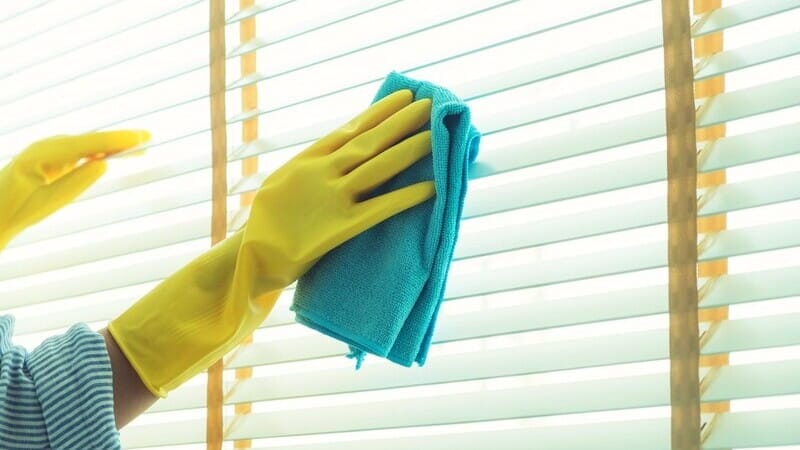 woman hand with yellow gloves holding a cloth to clean the blinds