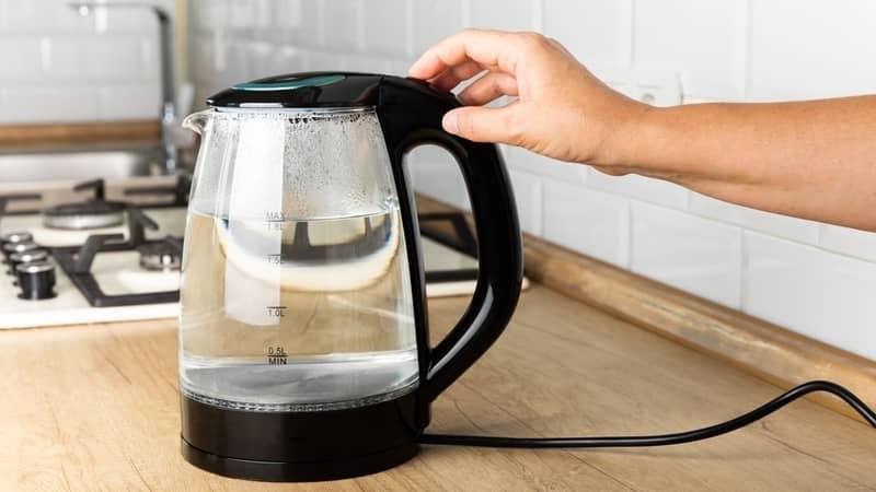 Close-up of a woman pressing the power switch on an electric kettle on a table