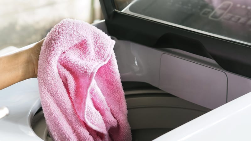 Hand holding pink towel over a top load washing machine