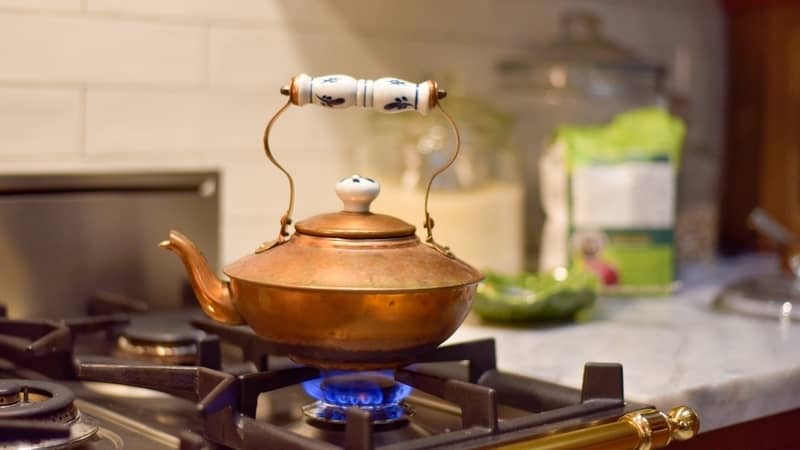 vintage copper tea kettle heating up water on a stove top