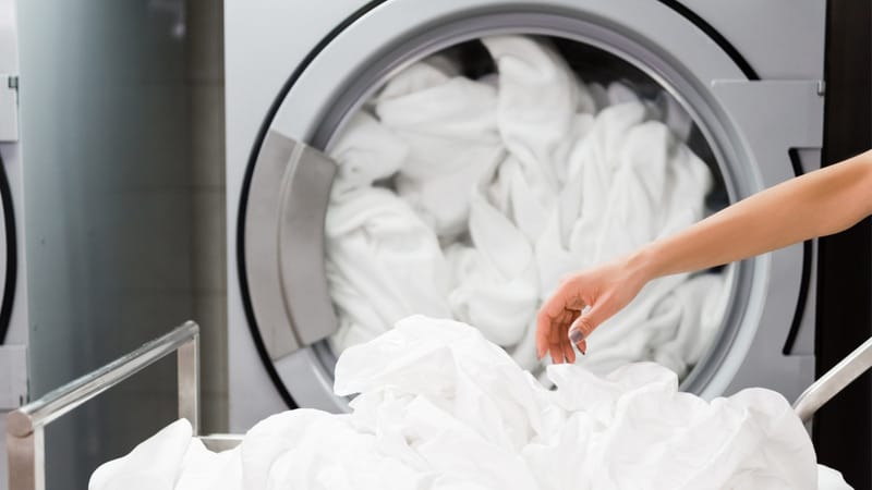 female hand near white bed sheets in laundry