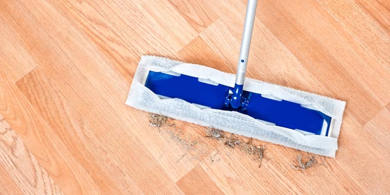 Image of a modern floor dusting mop being used to clean hair and dirt on a wooden laminate floor.