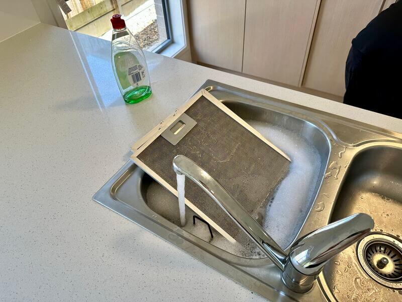 range hood filter soaking in the sink with water and soap