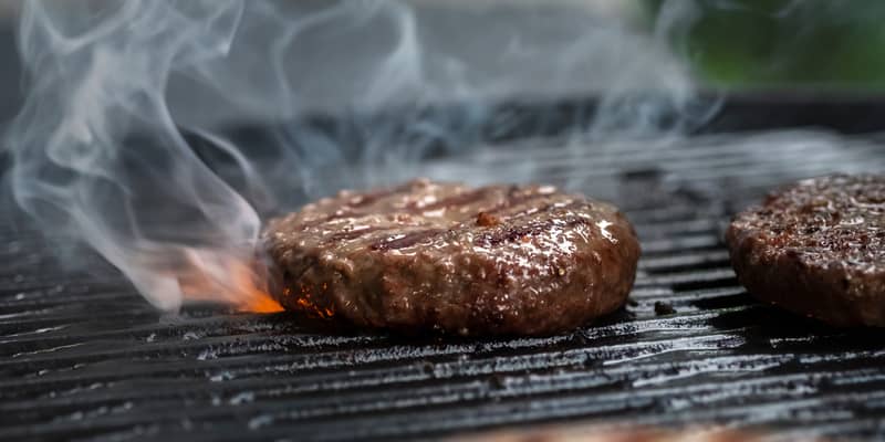 Hamuburgers cooking on gas grill outdoors.