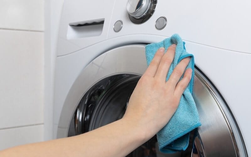 Hand wiping front load washer exterior with blue microfibre cloth