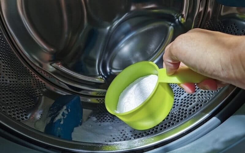 hand pouring a cup of baking soda inside a front loading washer