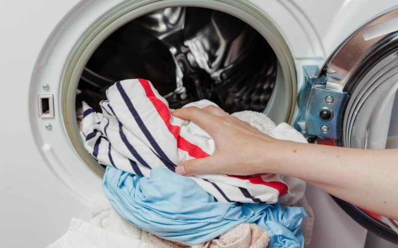 Hands pull wet, clean clothes out of a front-loading washing machine. 