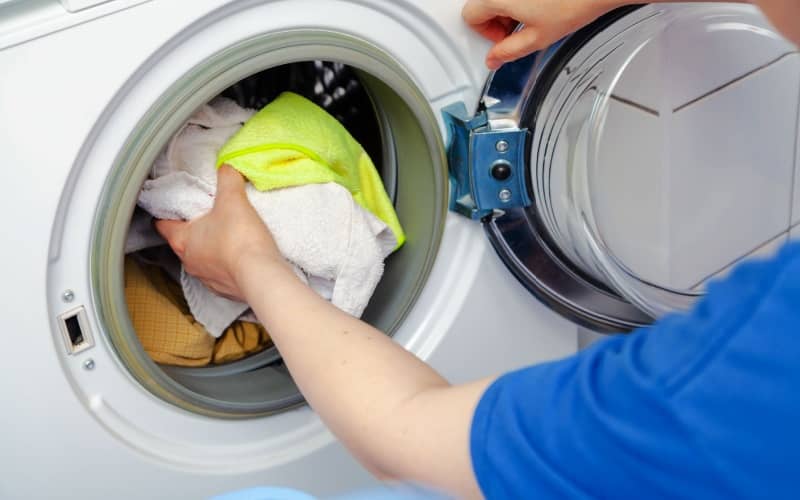 Hands putting dirty laundry in a front-loading washing machine