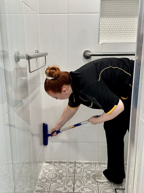 Hollie using a scrub brush to clean shower tile grout