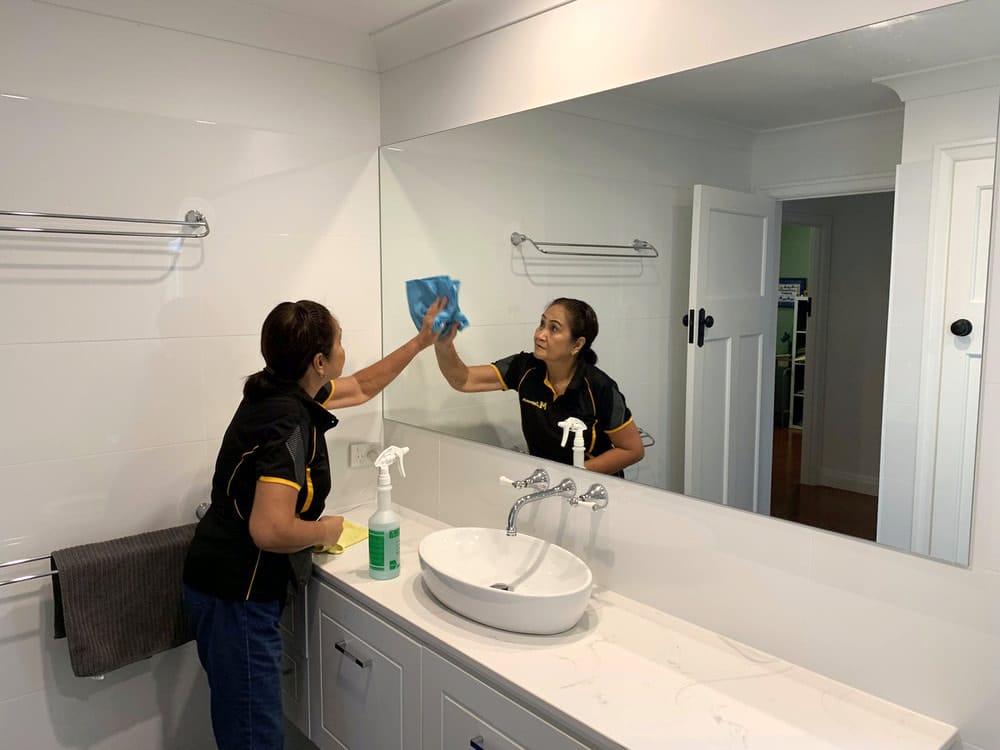 Professional cleaner wiping a large bathroom mirror above the sink