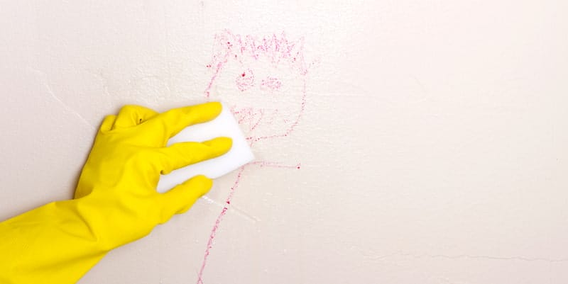 hand with yellow gloves cleaning crayola marks on the wall