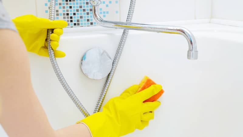 A woman cleaning bath at home. Female washing bathtub and faucet