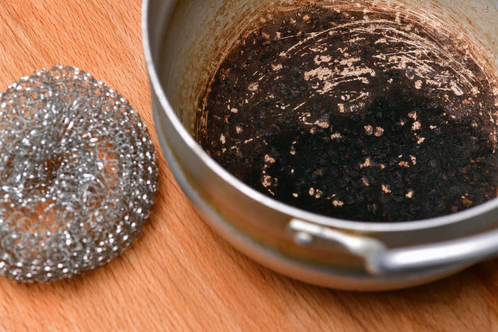 A spoiled burnt pan with a steel wool lies on a wooden Boar