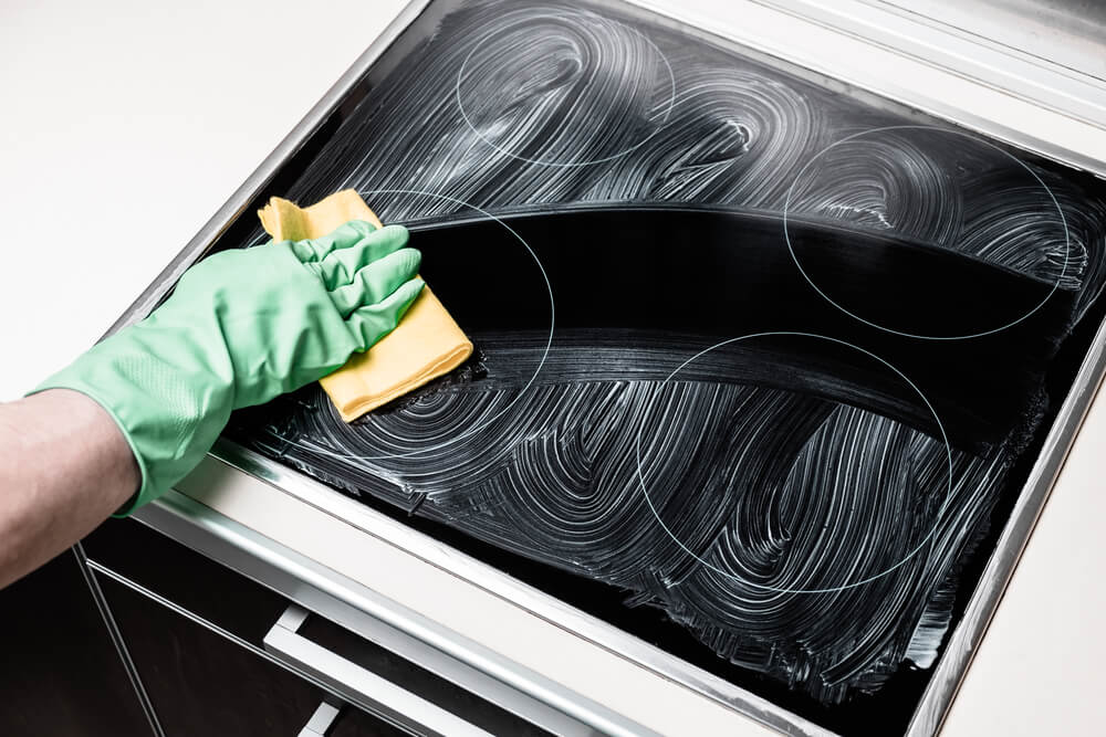 Man's hand in green protective glove with yellow rag cleaning cooker at home kitchen