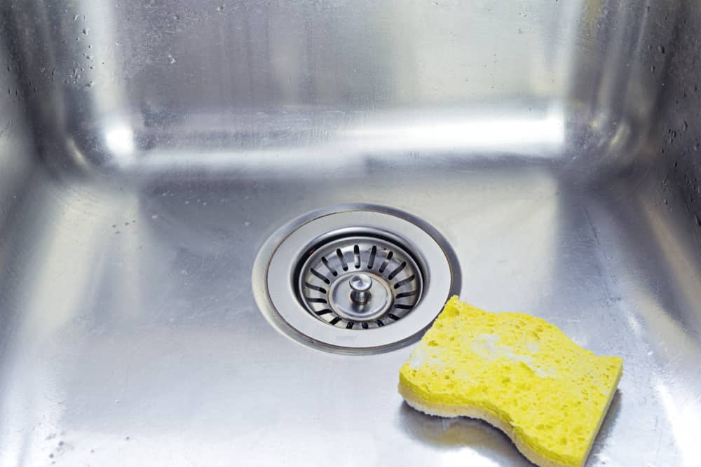 Cleaning polished stainless shiny sink with scrub sponge in kitchen