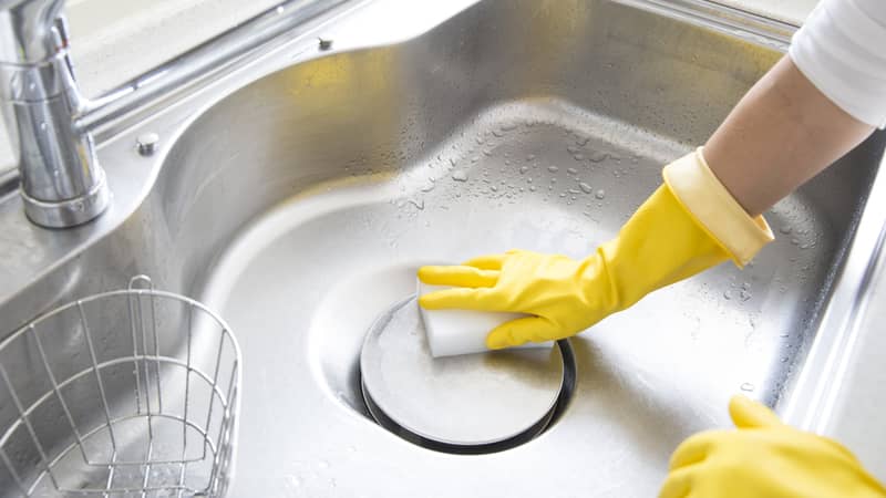 female hands with yellow gloves cleaning the kitchen sink