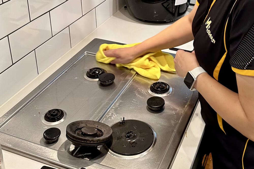 Professional cleaner wiping the surface of a stainless steel cooktop